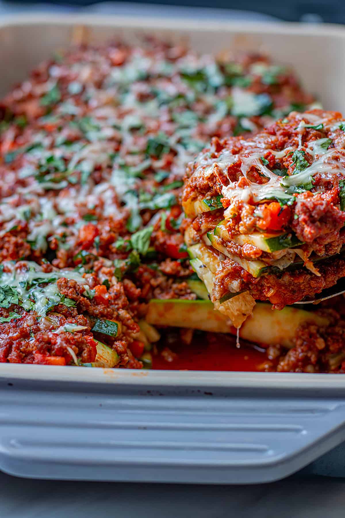 A spatula scooping out a slice of zucchini lasagna with ground meat and tomato sauce. 
