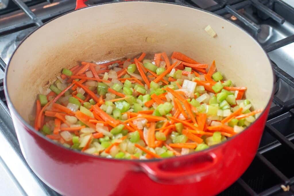 A large dutch oven with carrots celery and onions cooking on a stove. 