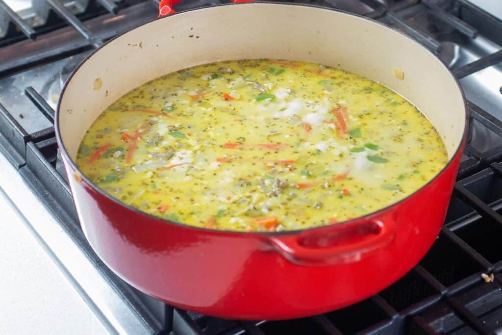 A large dutch oven with a sausage, potato and kale soup simmering on a stove.