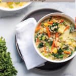 A bowl of soup sitting on a plate with words that say sausage, kale and potato soup.