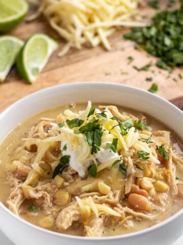 A bowl full of a chicken chili topped with white cheddar cheese.