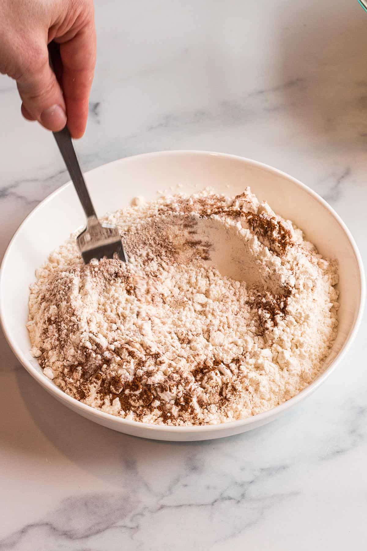 Small bowl with flour, cinnamon, salt and baking soda being mixed with a fork. 