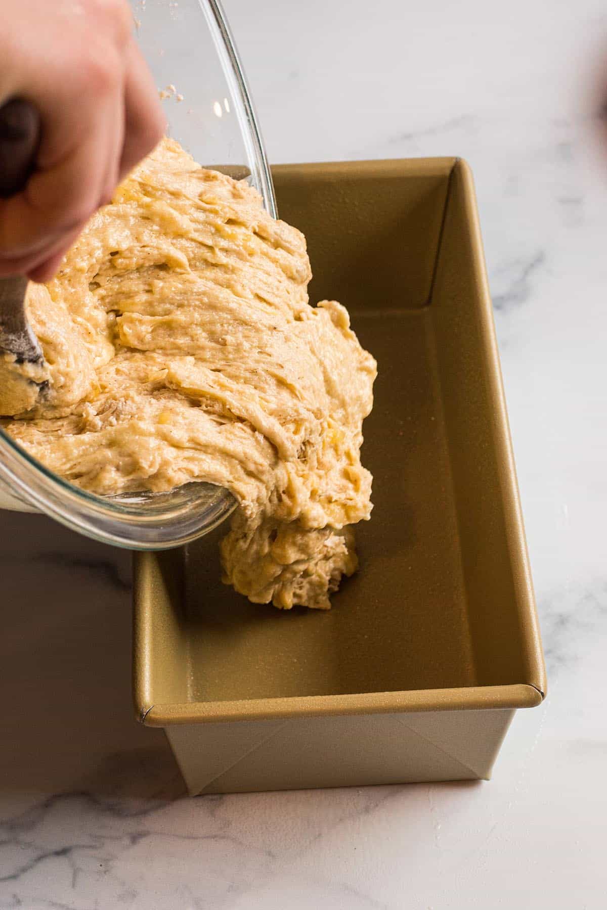 Banana bread batter being poured into a prepared loaf pan. 