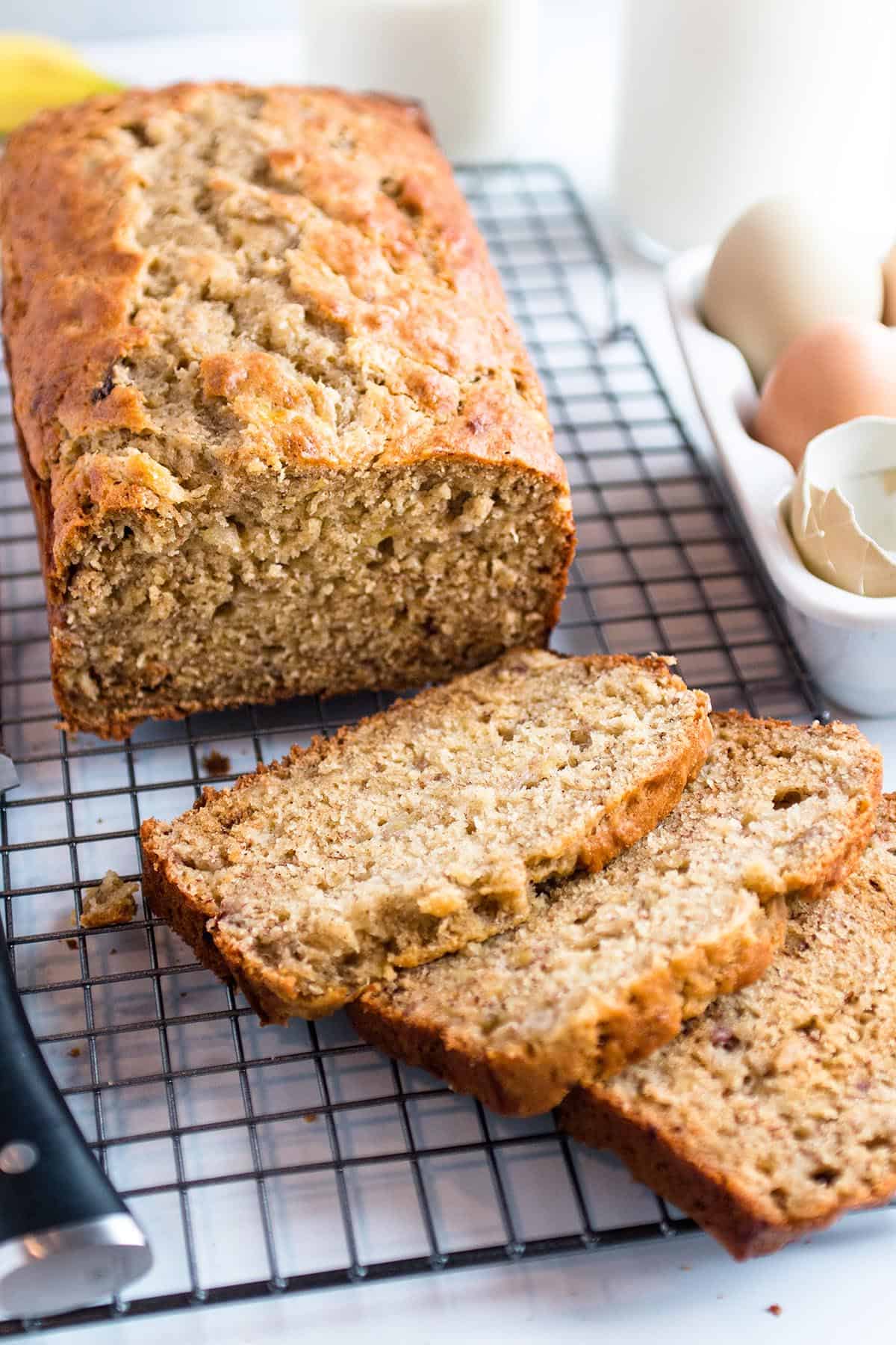 A loaf of banana bread on a cooling rack cut into slices.