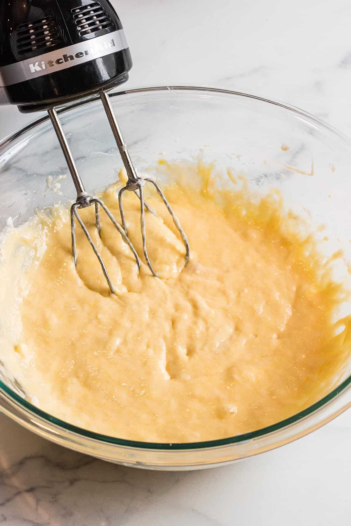 Glass bowl with banana bread batter being mixed with a hand mixer. 
