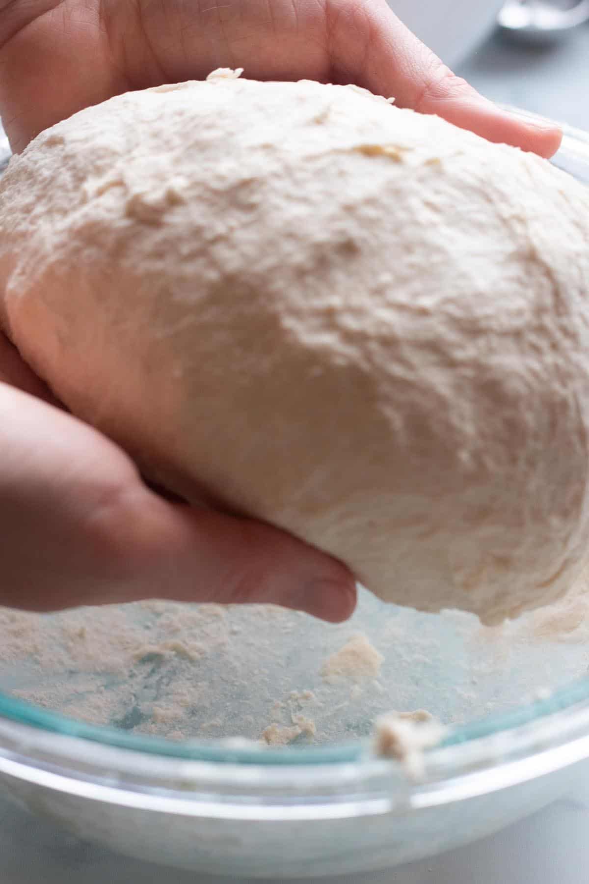 Two hands forming a ball of sourdough naan. 