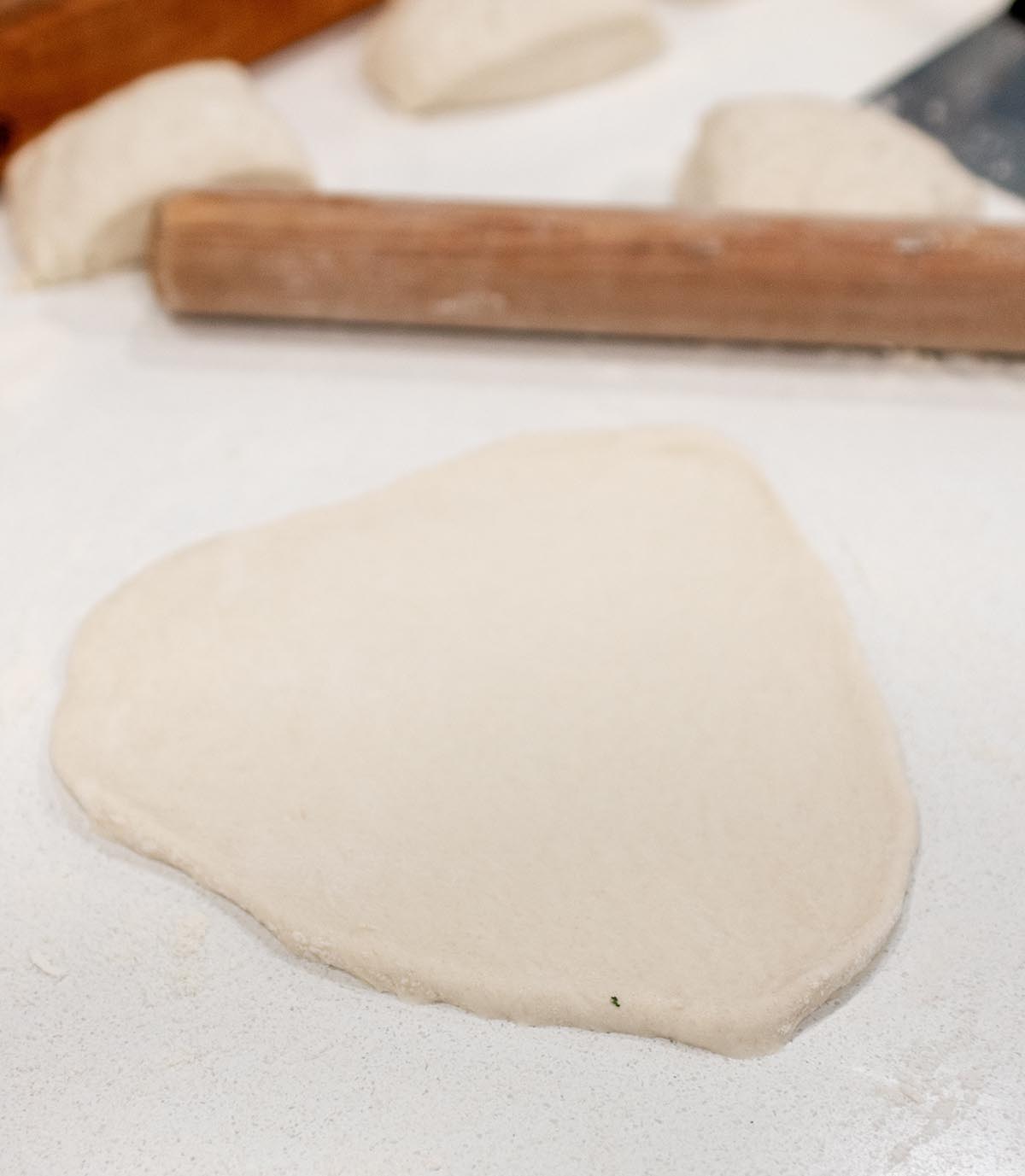 A piece of sourdough naan being rolled out onto the counter. 