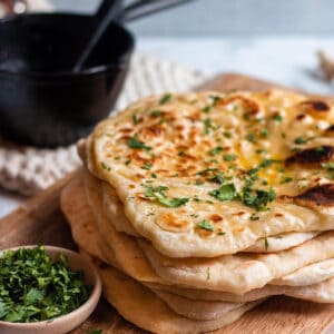 stack of sourdough naan on a wood board with cilatro and cast iron butter melter.