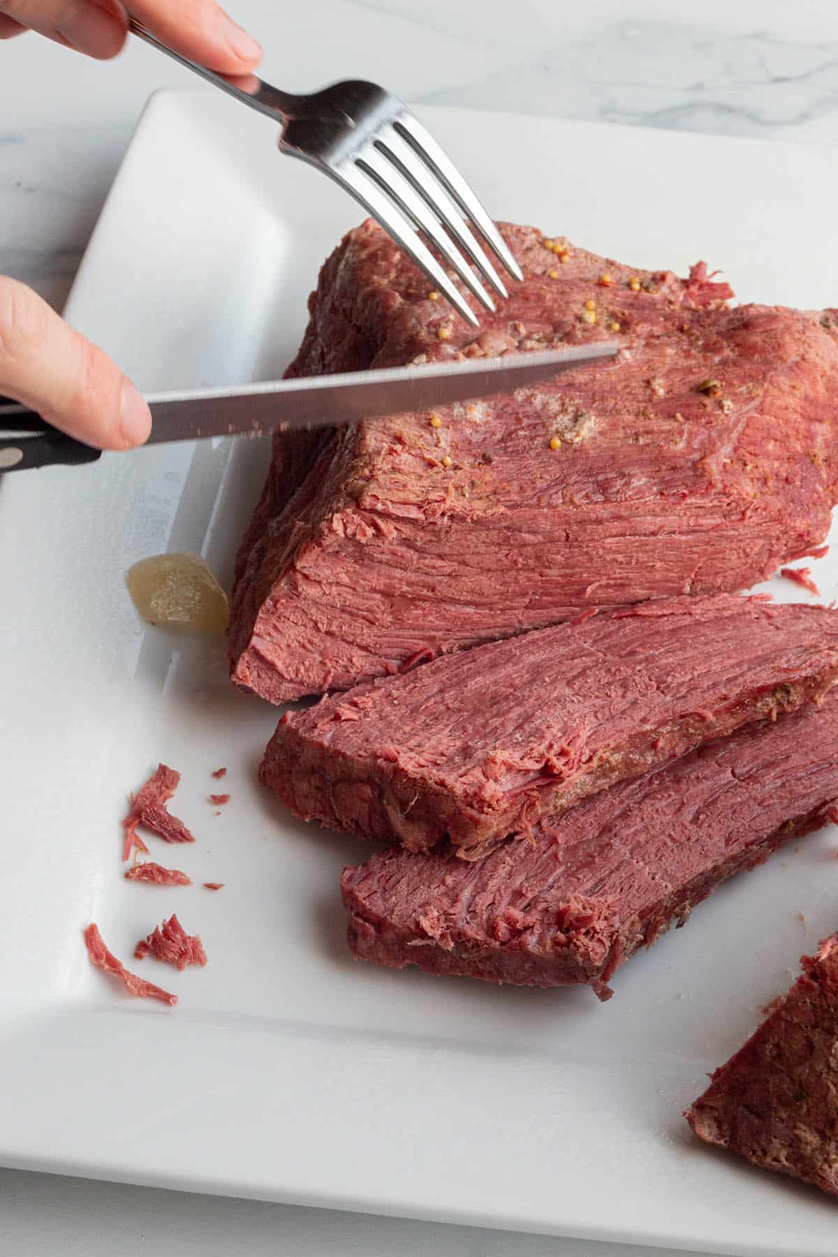 A plate with a corned beef brisket being cut into slices.
