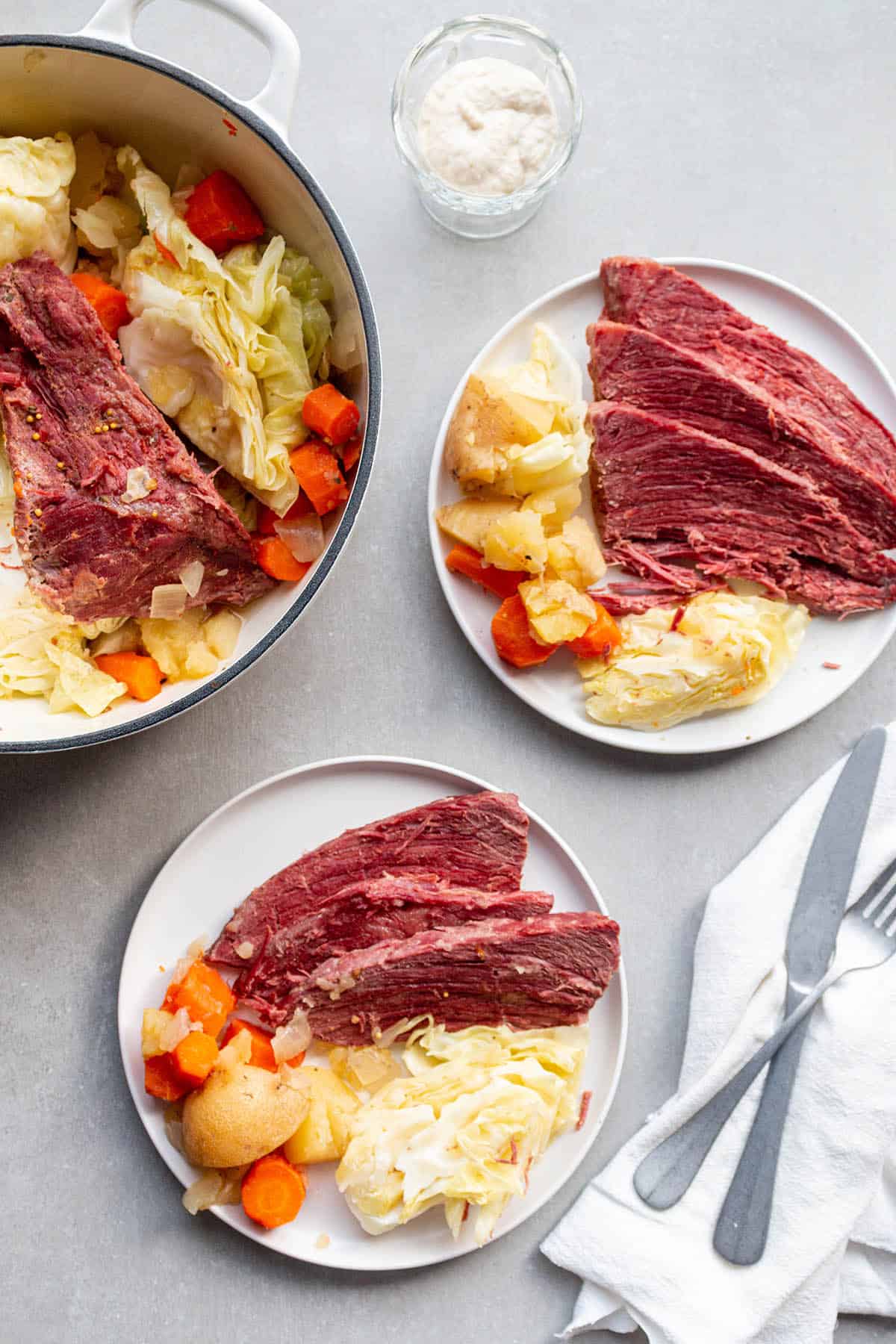 Two plates with servings of corned beef, cabbage, carrots and potatoes with a Dutch Oven full of the roast. 
