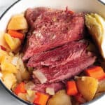 A white dutch oven pot with a corned beef brisket, cabbage, potatoes and carrots.