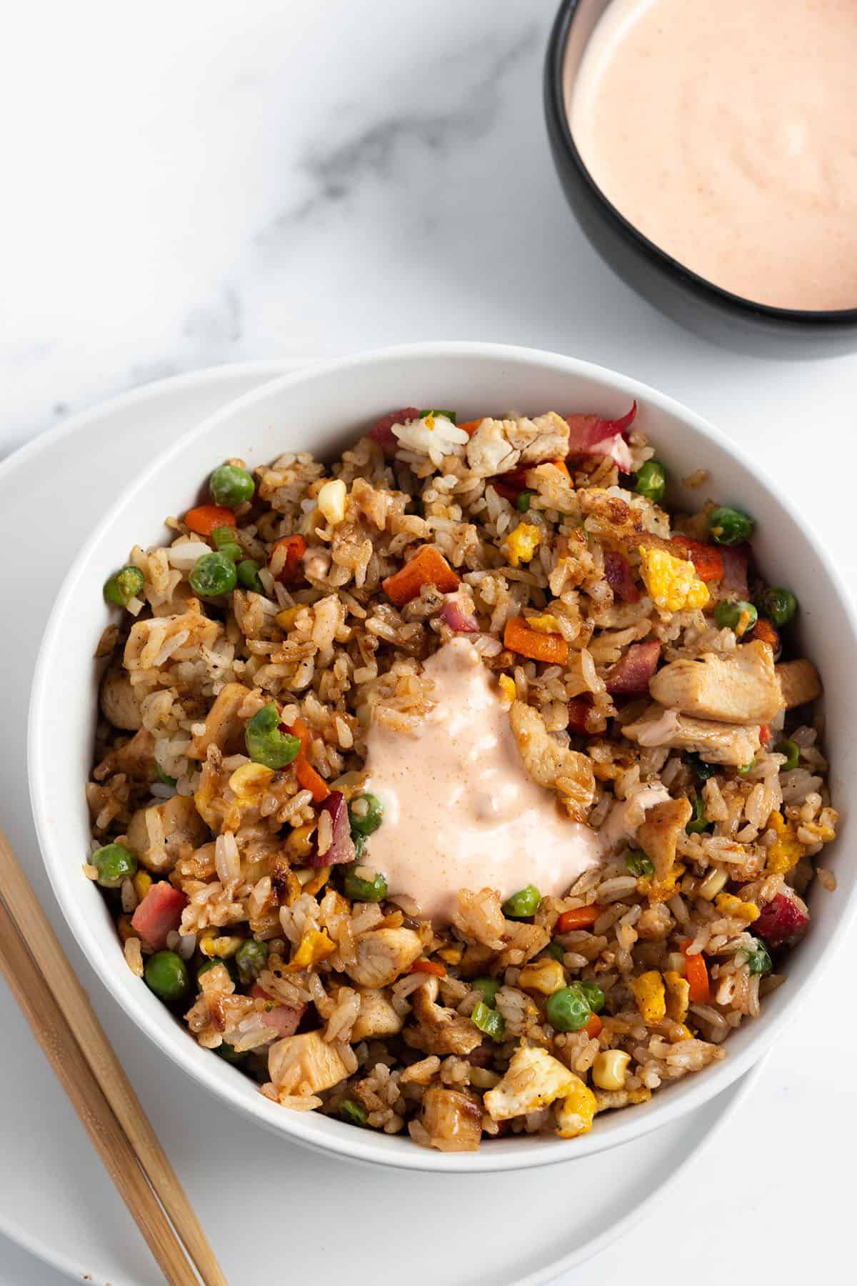 A bowl of fried rice with yum yum sauce on top and in a bowl. 