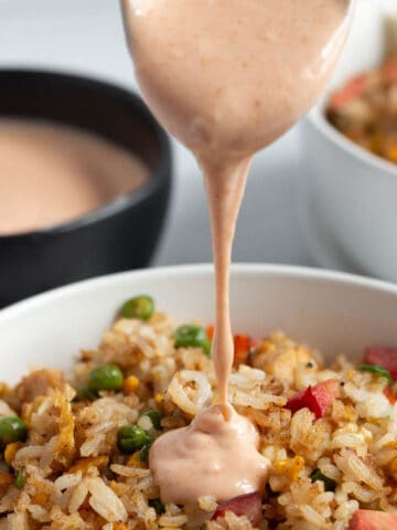 A bowl of fried rice with yum yum sauce being poured on top.