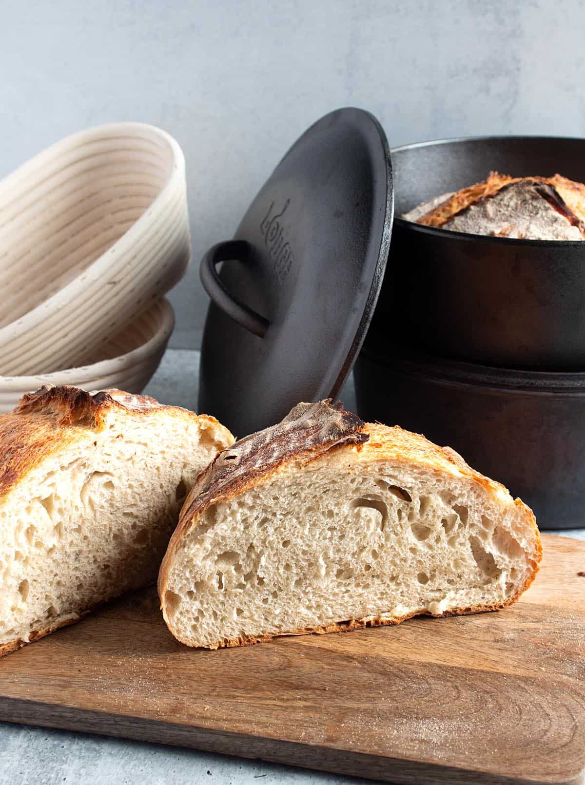 Loaf of sourdough bread with bannetons and a cast iron dutch oven with a loaf inside.