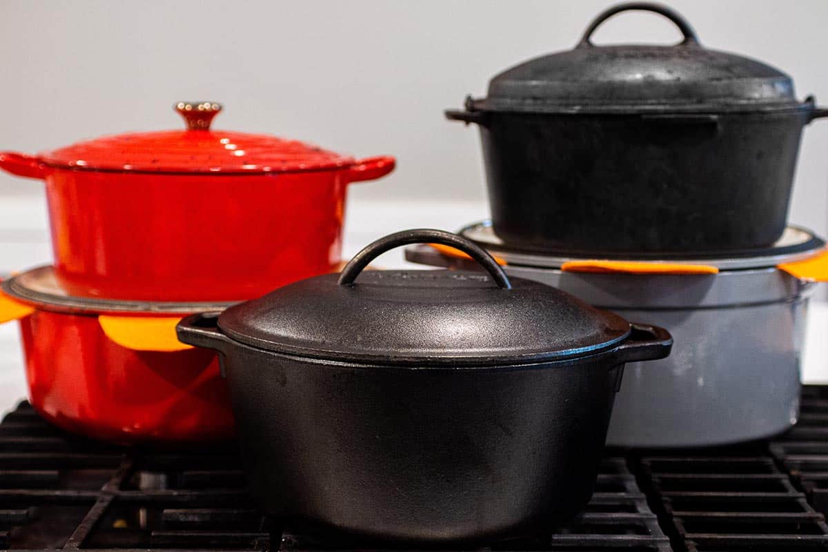 A collection of dutch ovens. Two red Le Creuset, two cast iron 5qt, and a large grey one. 