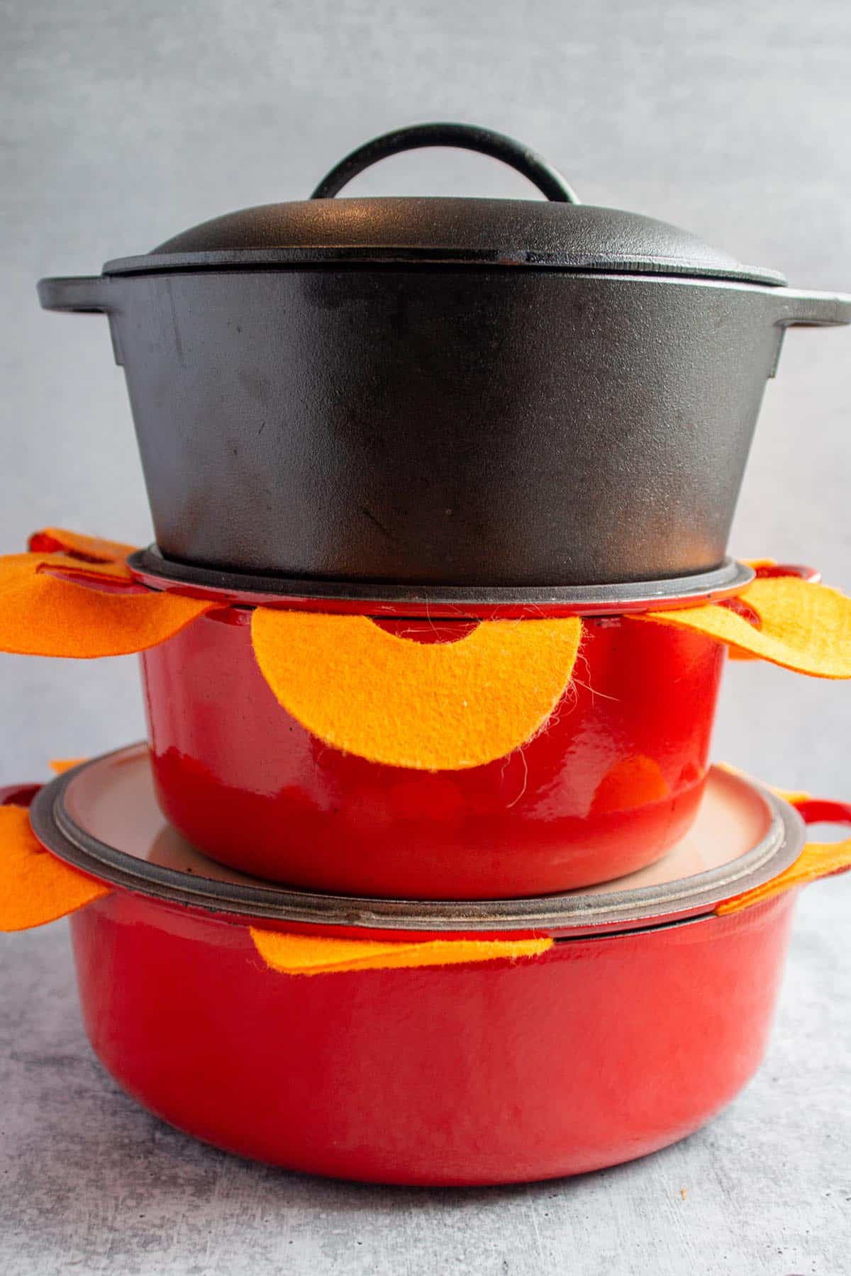 A stack of dutch ovens. Two red Le Creuset and one Lodge Cast iron. Felt separators in-between each one.  