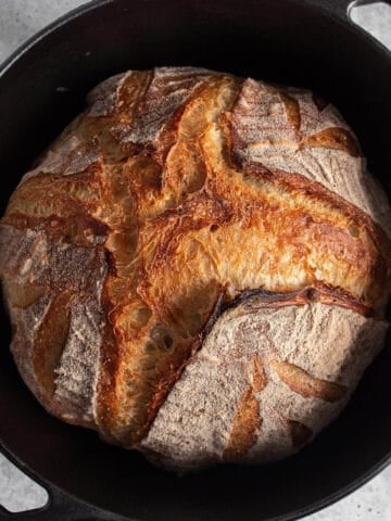 A cast iron Dutch Oven with a freshly baked loaf of sourdough bread.