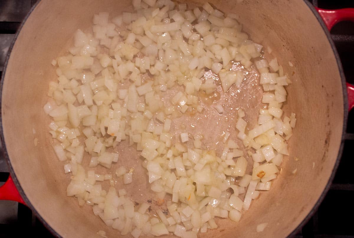Dutch oven with diced up onions simmering in olive oil.