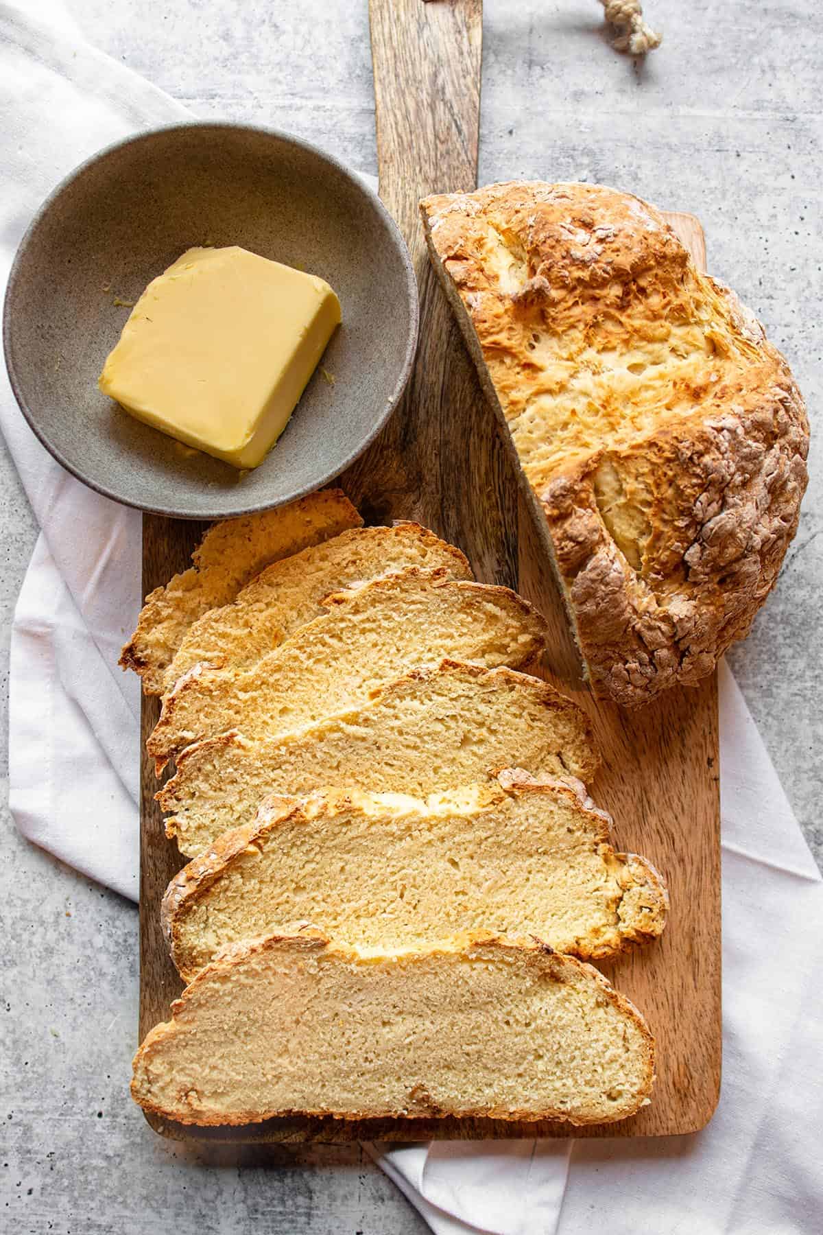 A wooden board with half a loaf of Irish soda bread with slices and a bowl of butter.