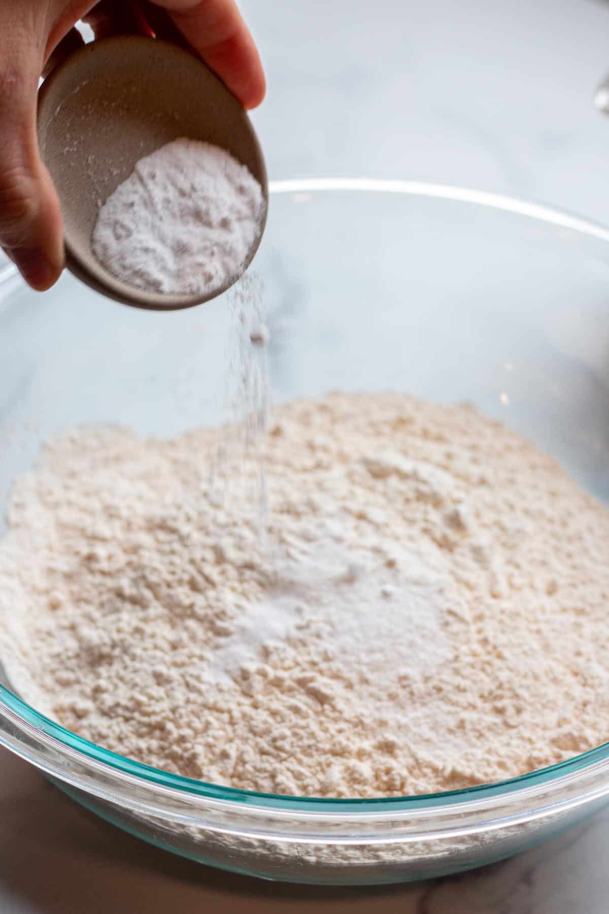 Baking soda being added to a bowl of flour.