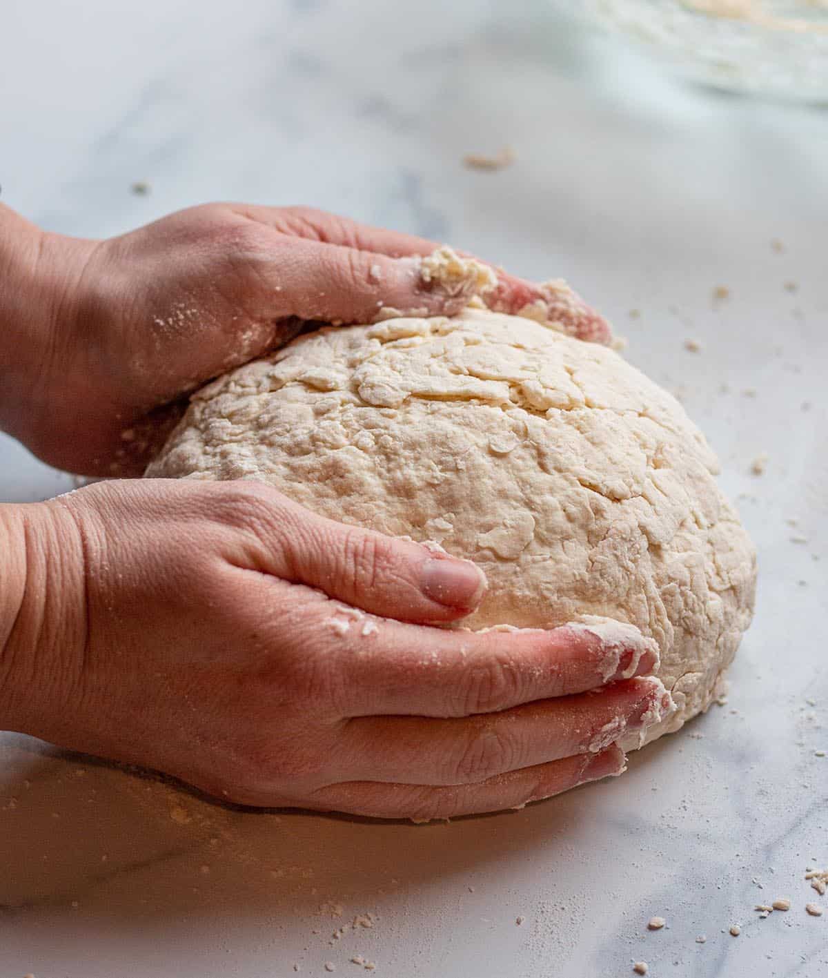 Two hand forming a ball of Irish soda bread. 
