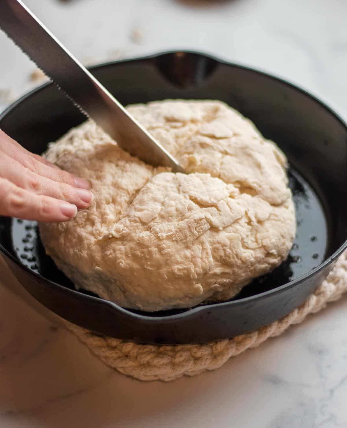 A knife cutting a loaf of soda bread in a cast iron skillet.