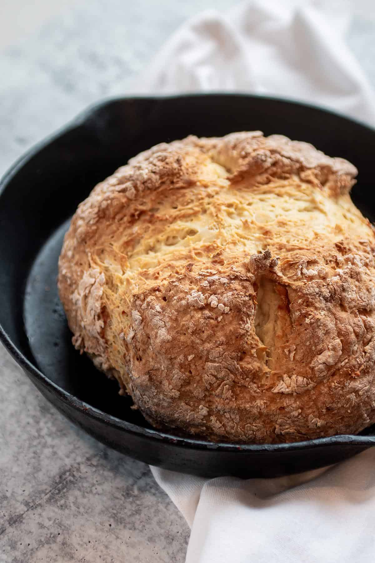 A cast iron pan with a loaf of soda bread.