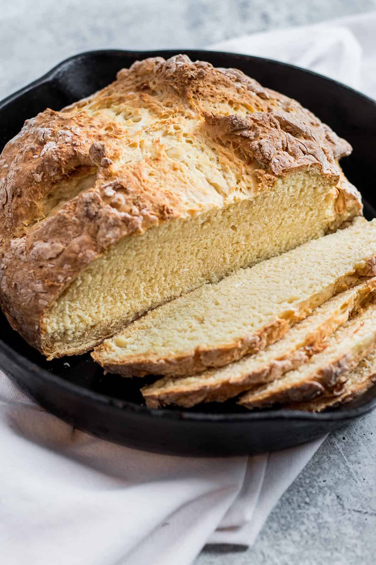 A fresh loaf of Irish Soda bread with slices in a cast iron pan.