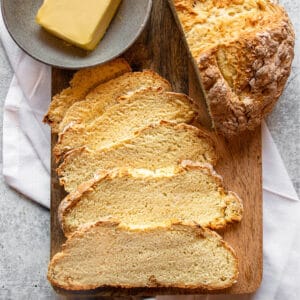 A wooden board with slices of Irish soda bread with the other half of the loaf and a bowl of butter.