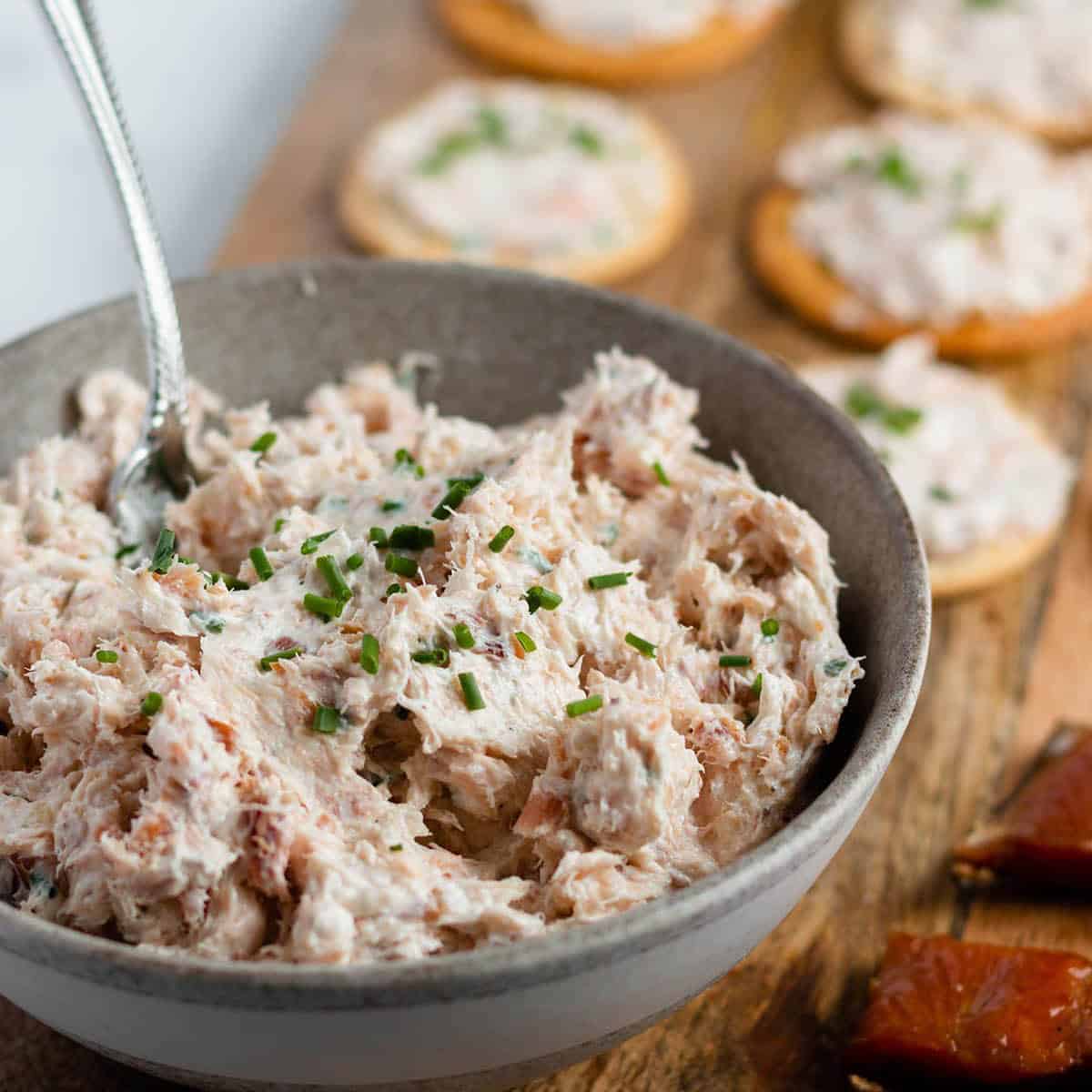 A bowl with homemade smoked salmon dip and crackers all on a wooden board. 