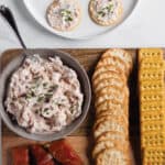 Wooden board with a bowl of smoked salmon dip and crackers.