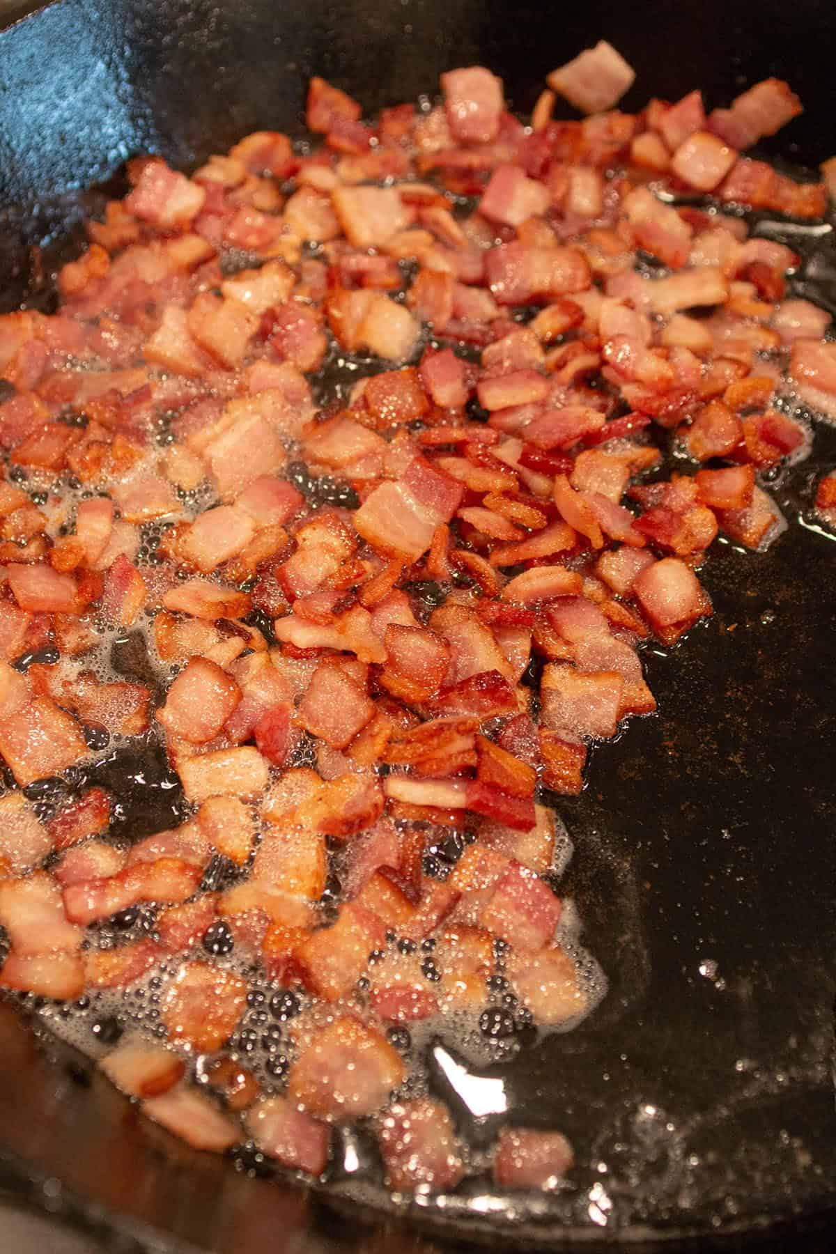 A large cast iron skillet with diced bacon rendering. 