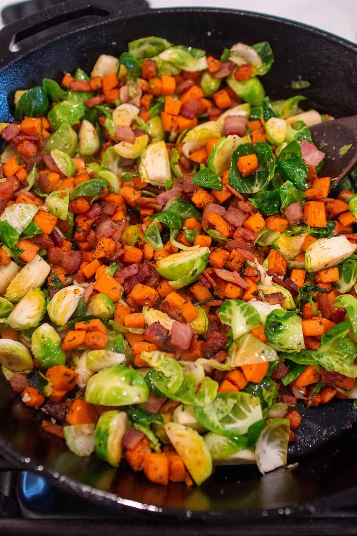 A large cast iron with cooked sweet potatoes, brussels sprouts and bacon. 