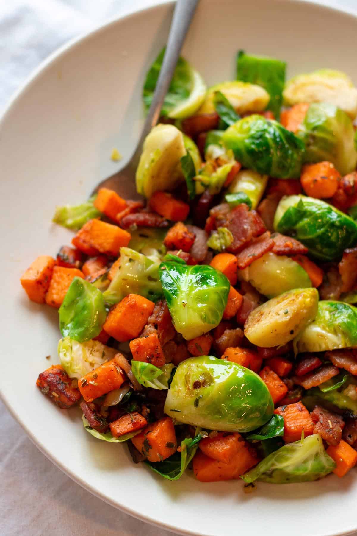 Plate with cooked sweet potatoes brussels sprouts and bacon. 