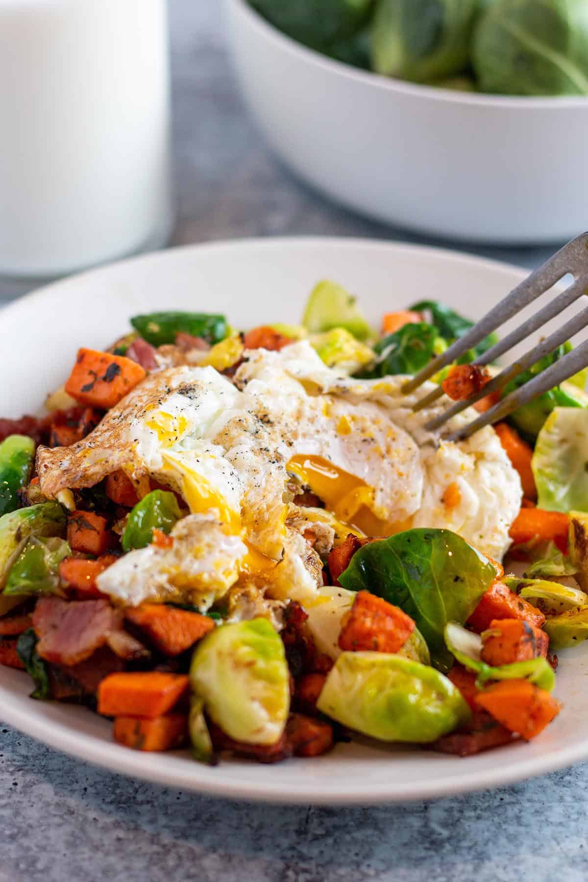 A plate with sweet potato and brussels sprouts breakfast hash with a fried egg on top. 