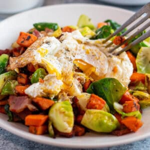 A plate with a sweet potato and brussel sprout mix with a fried egg on top.