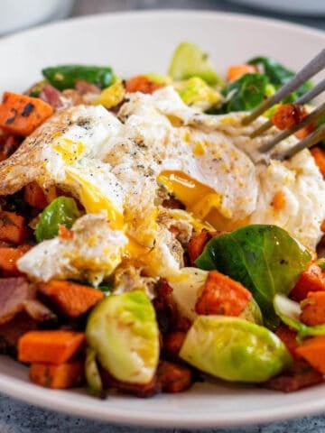 A plate with a sweet potato and brussel sprout mix with a fried egg on top.