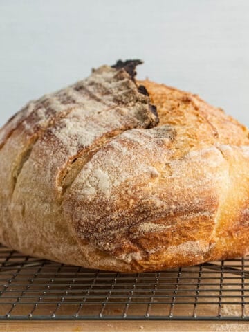 A fresh loaf of sourdough bread sitting on a cooling rack.