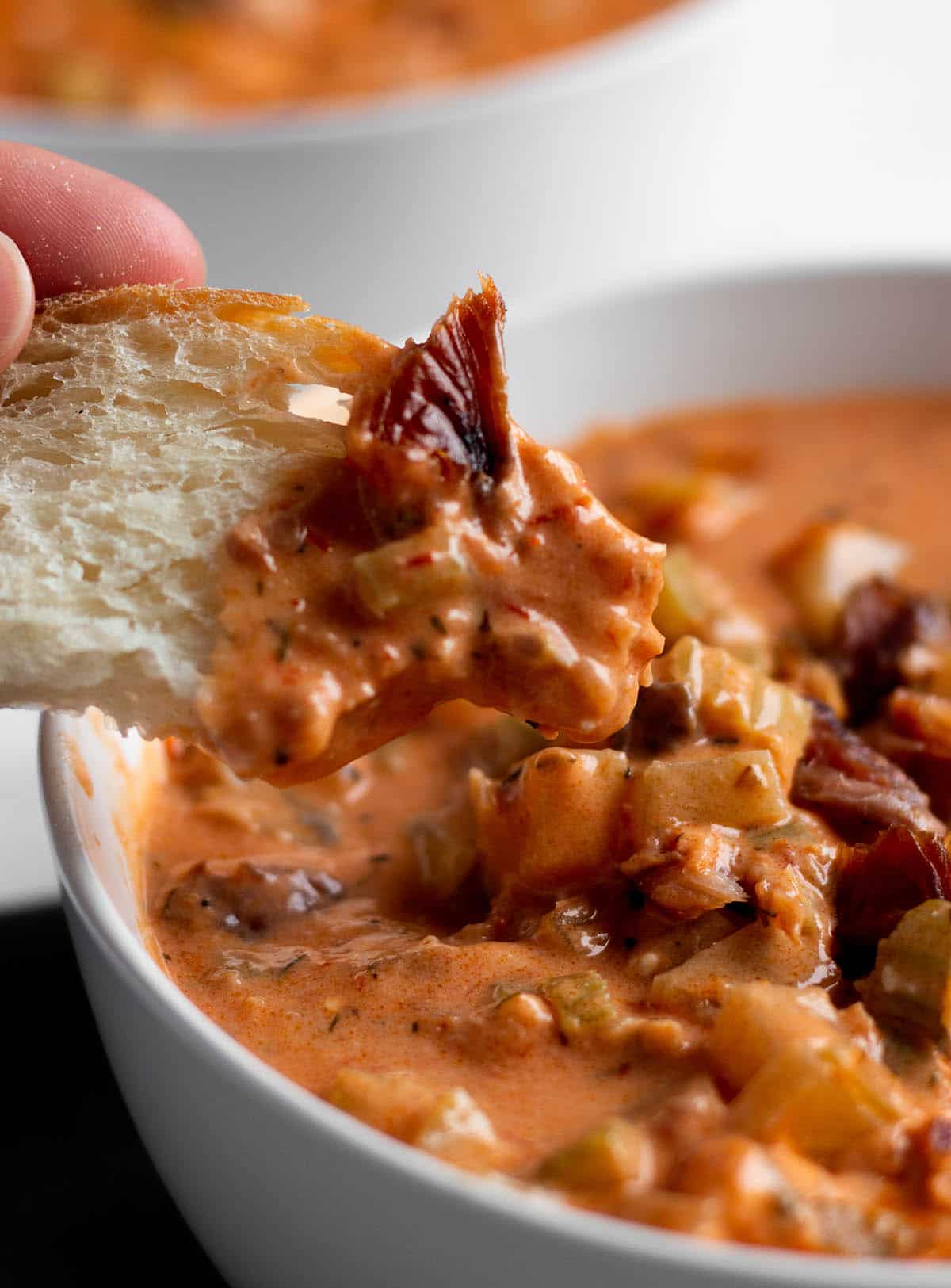 A piece of sourdough bread being dipped in a bowl of smoked salmon chowder.