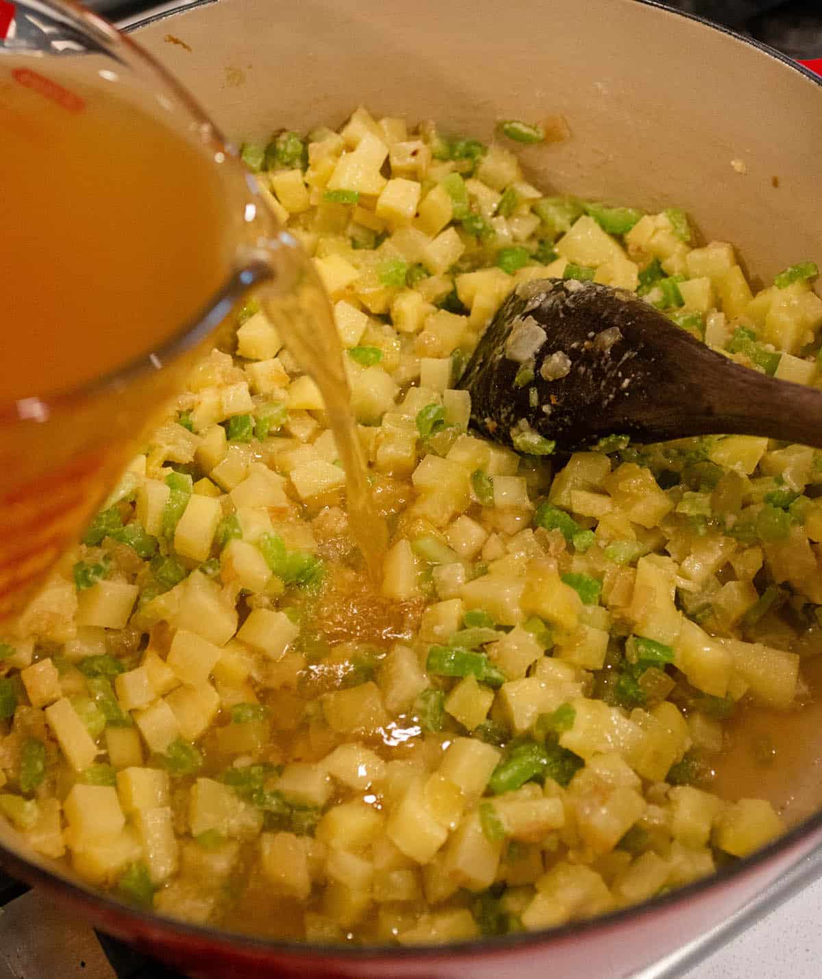 Dutch oven with potatoes and veggies with vegetable stock being poured in. 