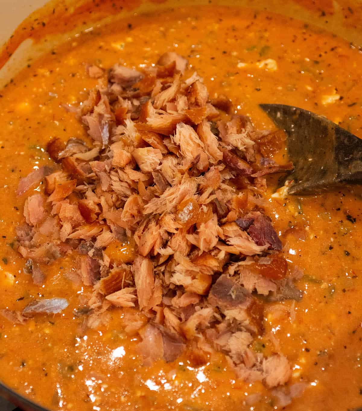 Chunks of smoked salmon being added to a chowder. 