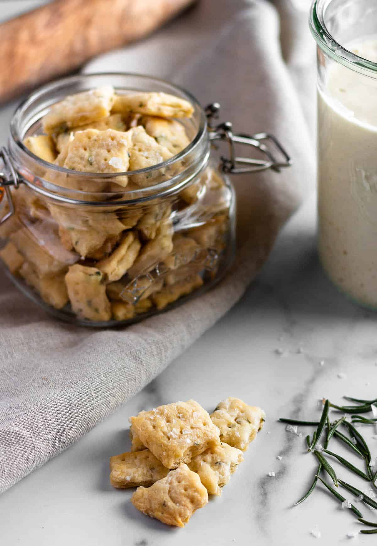 A jar full of homemade crackers with a jar of sourdough starter and a rolling pin. 
