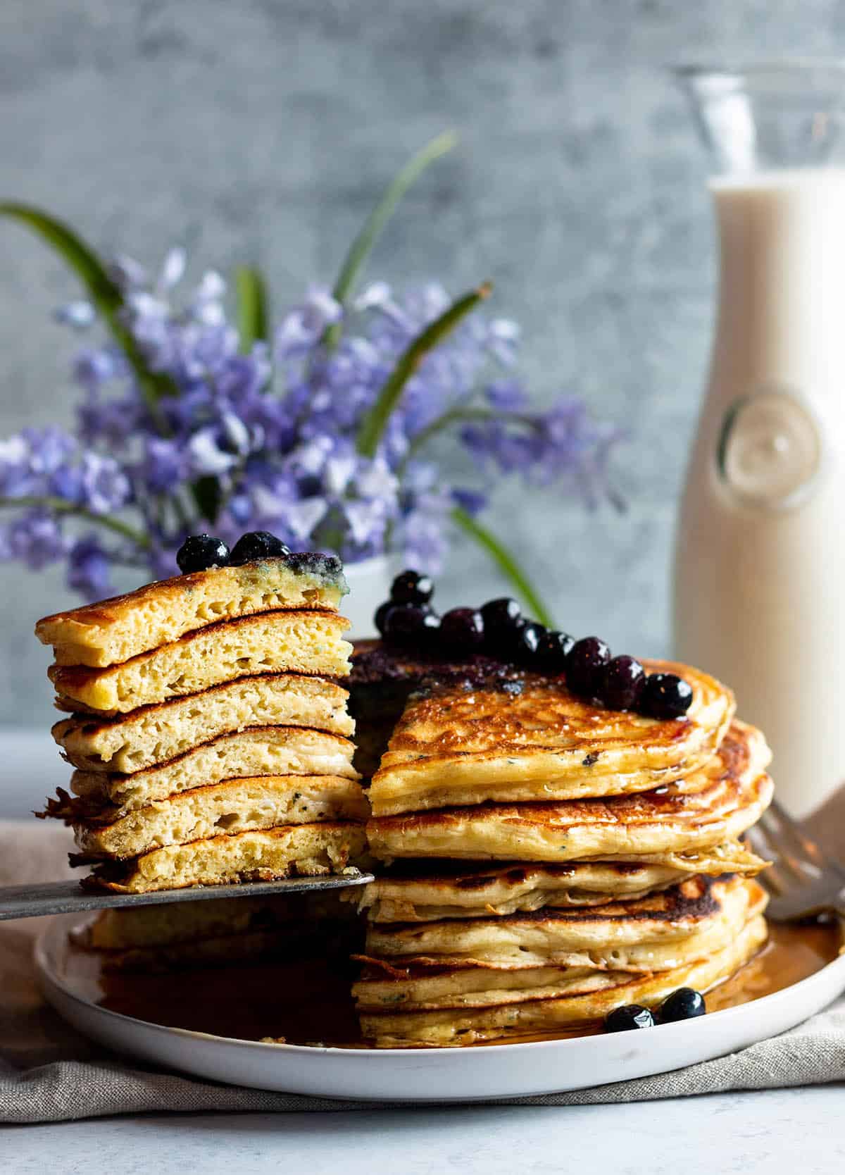 A stack of sourdough pancakes with blueberries on top and a large slice taken out to show the layers.