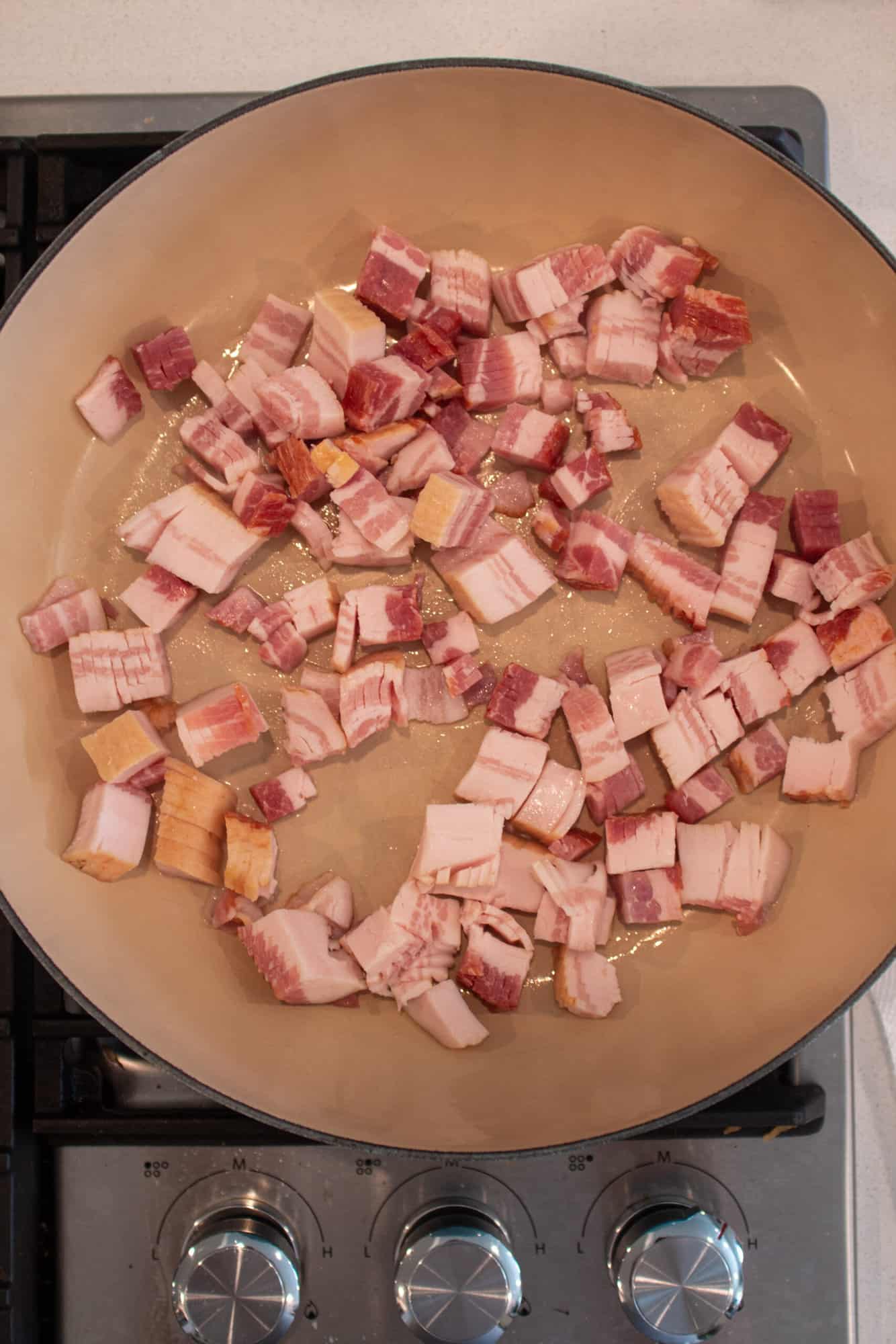 Diced bacon being cooked in a large skillet.