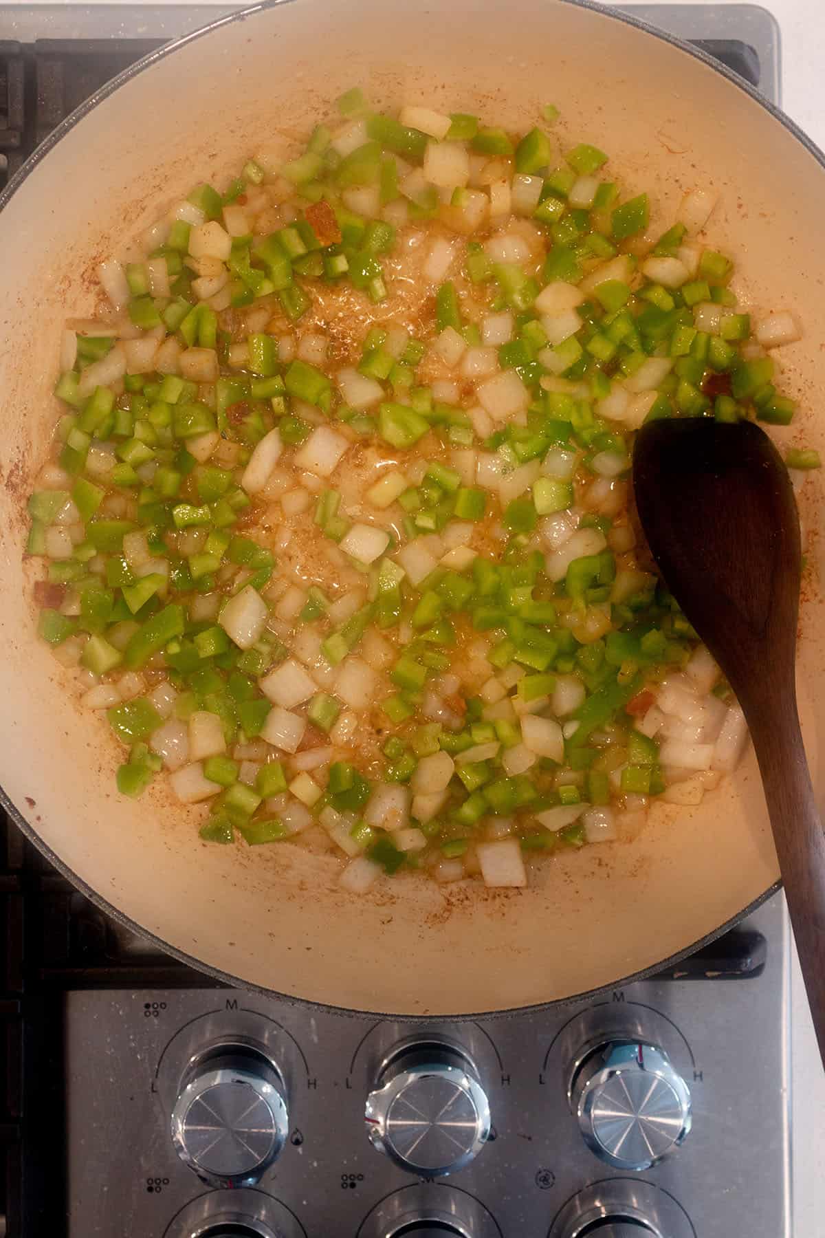 A large skillet with onions and green peppers being sautéed.