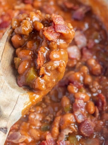 A large skillet with baked beans and a wooden spoon taking a scoop out.