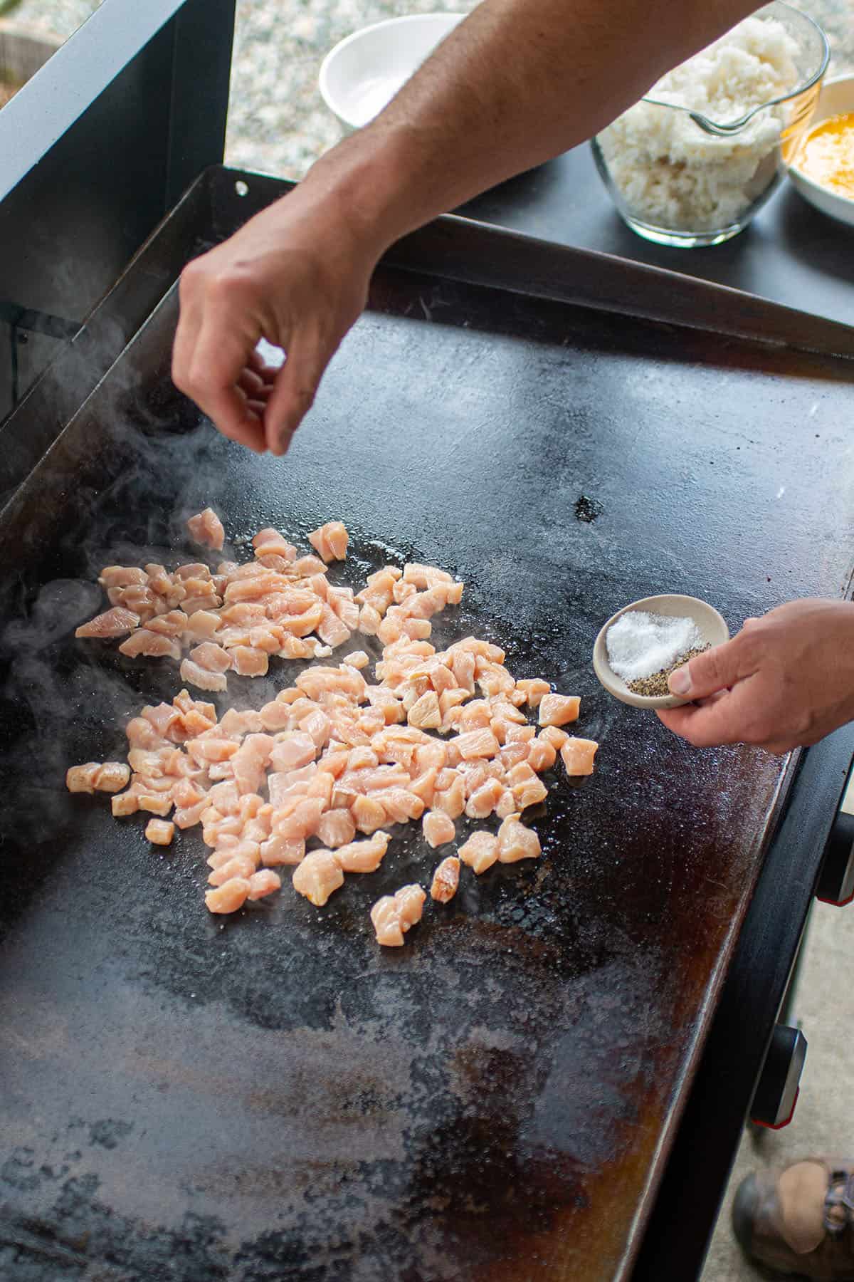 Diced chicken being seasoned with salt and pepper.
