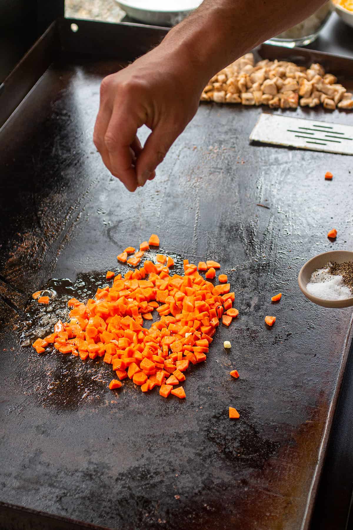 Diced carrots being seasoned with salt and pepper.