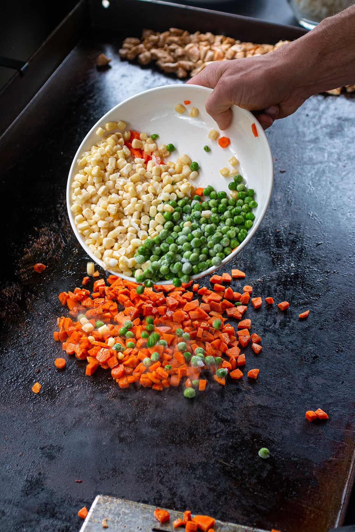 Frozen corn and peas being added to the cooked carrots.