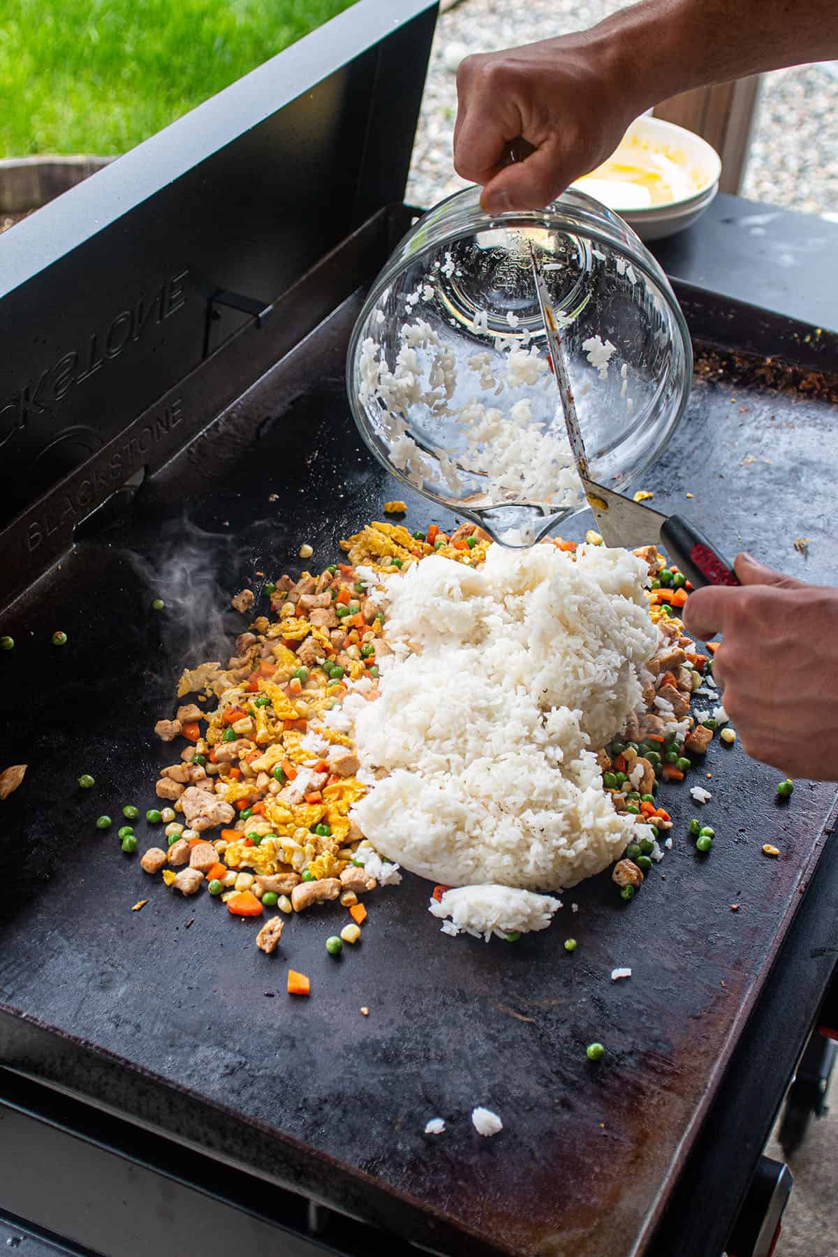 A pile of rice being added to the cooked veggies and chicken. 